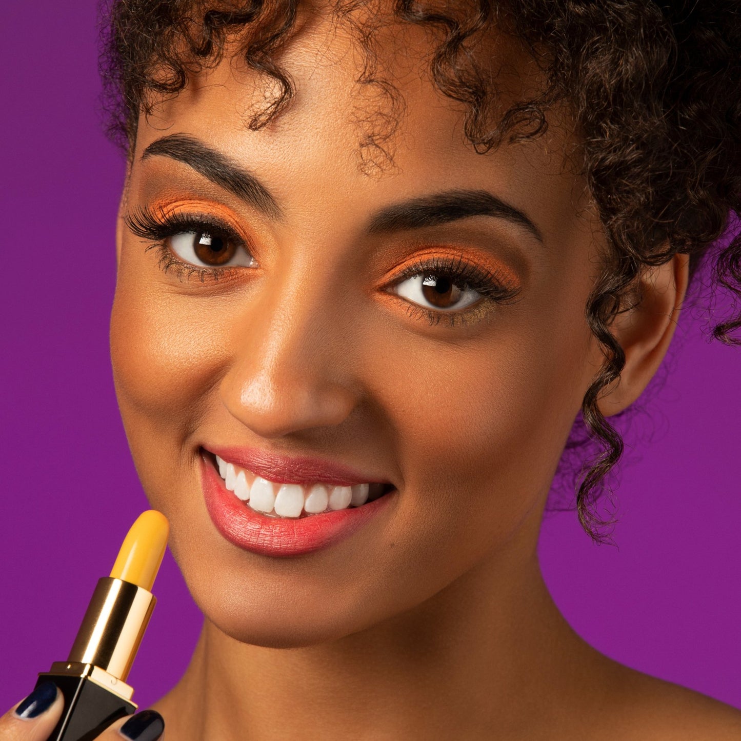 Woman applying yellow color-changing lipstick with coral lip stain finish