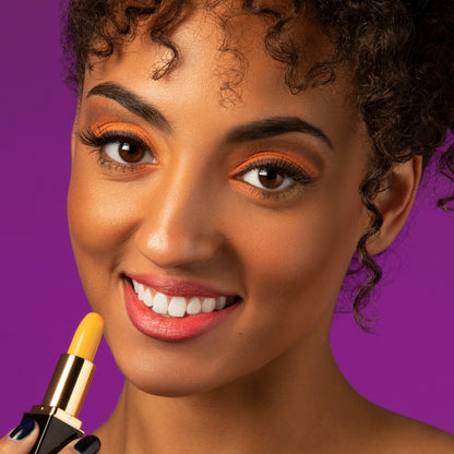 Woman applying yellow color-changing lipstick with coral lip stain finish